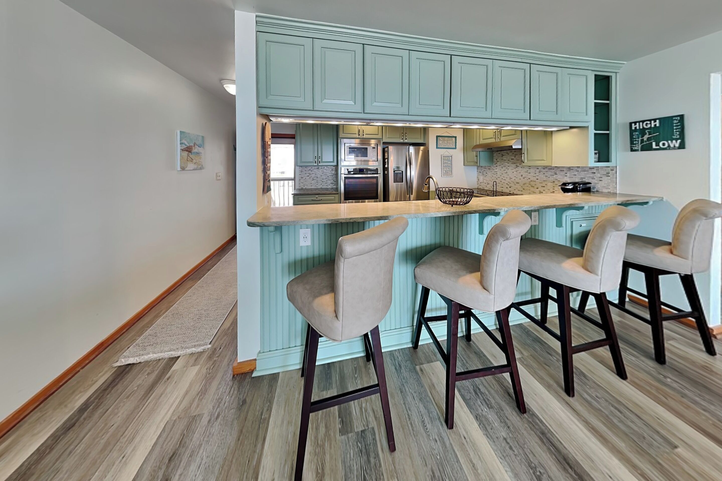 Una cocina con armarios color turquesa, una isla central con taburetes de bar y un refrigerador de acero inoxidable.