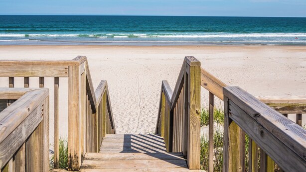 Une promenade en bois qui mène à une plage offrant une vue dégagée sur l’océan.