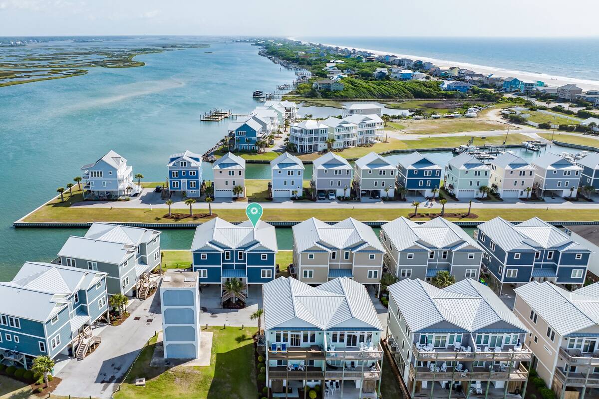 A coastal residential area with multiple two-story houses, a marina, and a beach in the background.