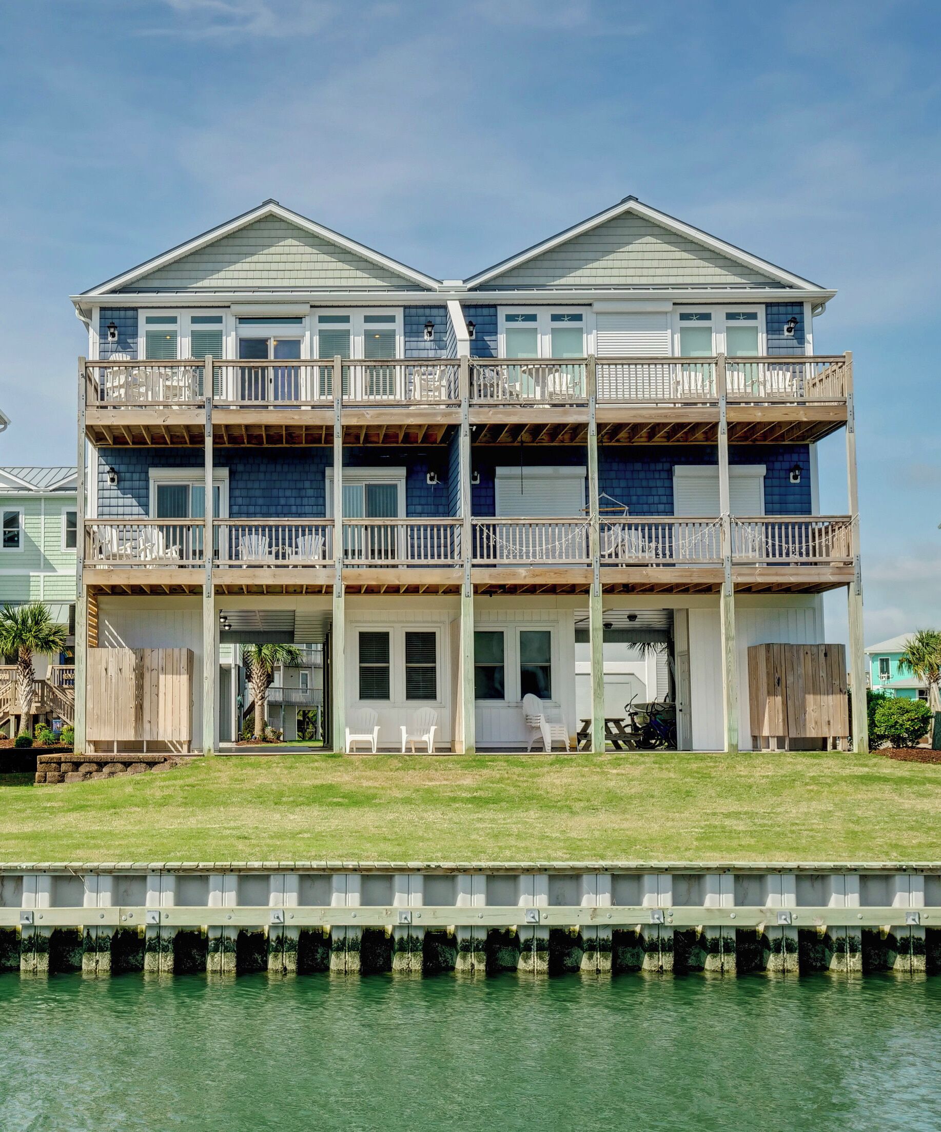 A two-story beachfront house with a balcony on each floor, a covered patio, and a view of the water.