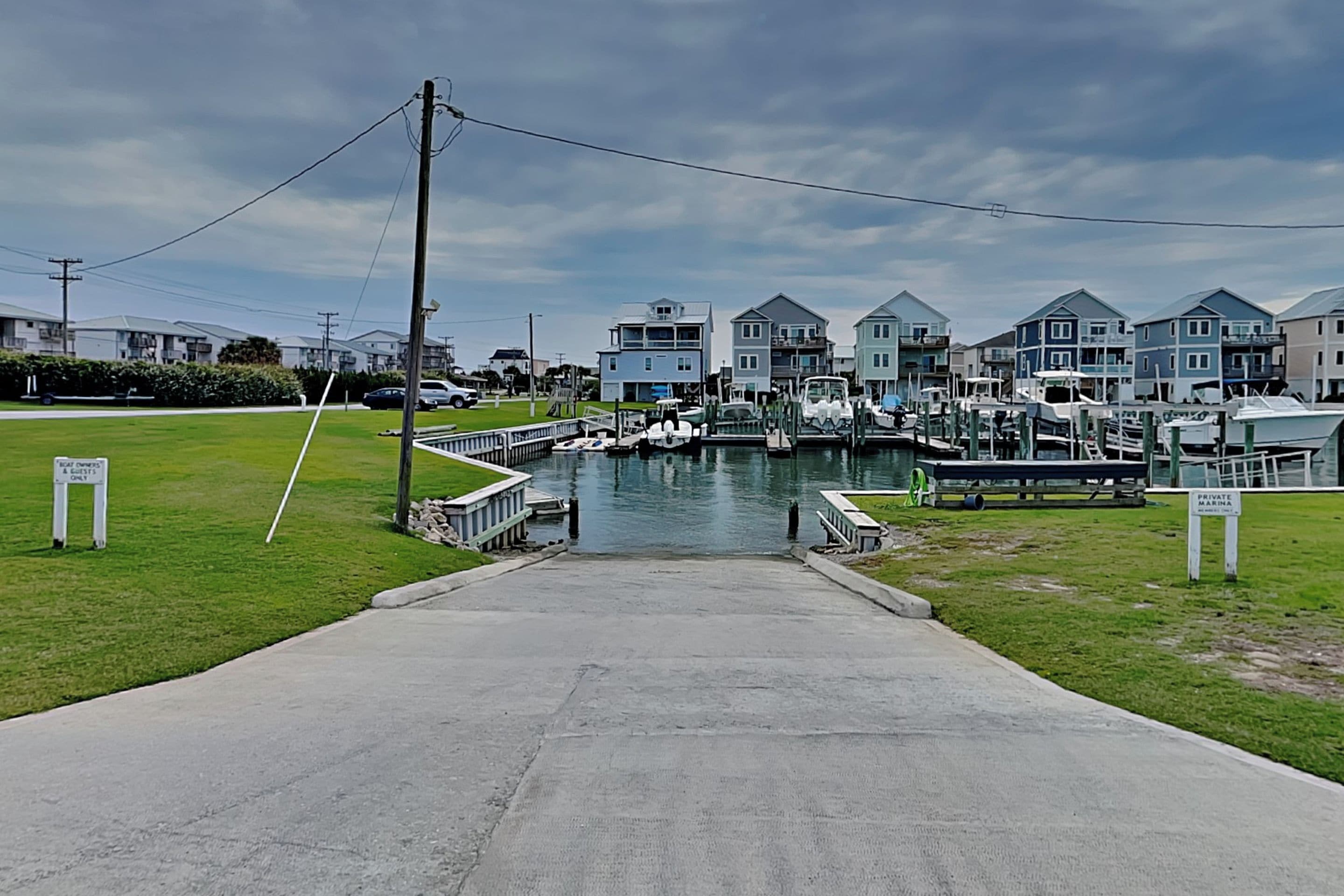 A marina with boats docked, a grassy area, and houses in the background.