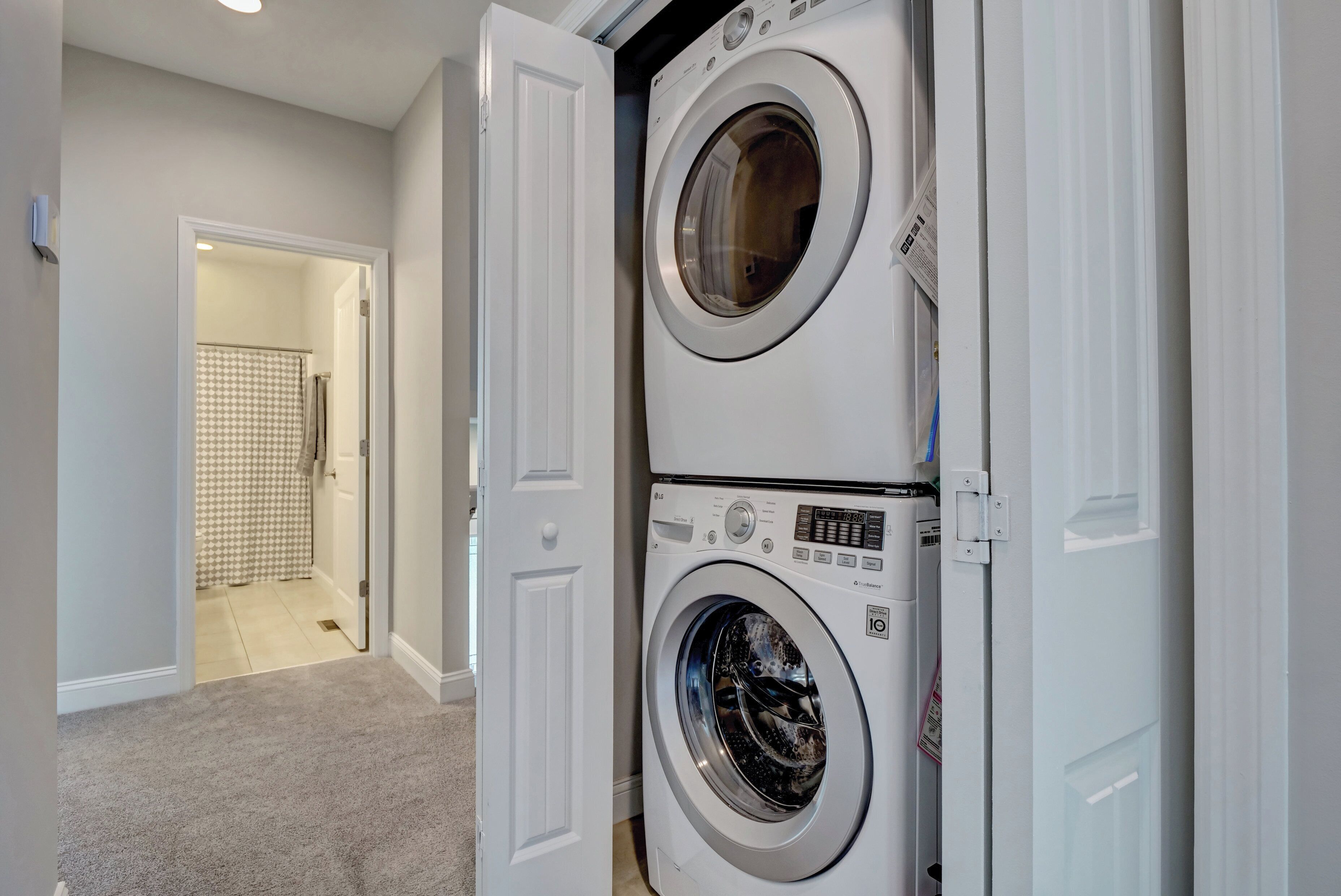 A laundry room with two stacked front-loading washing machines and a shower visible through an open door.