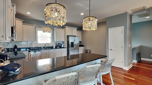 Une cuisine moderne avec des meubles blancs, un grand îlot central doté de tabourets et deux lustres.