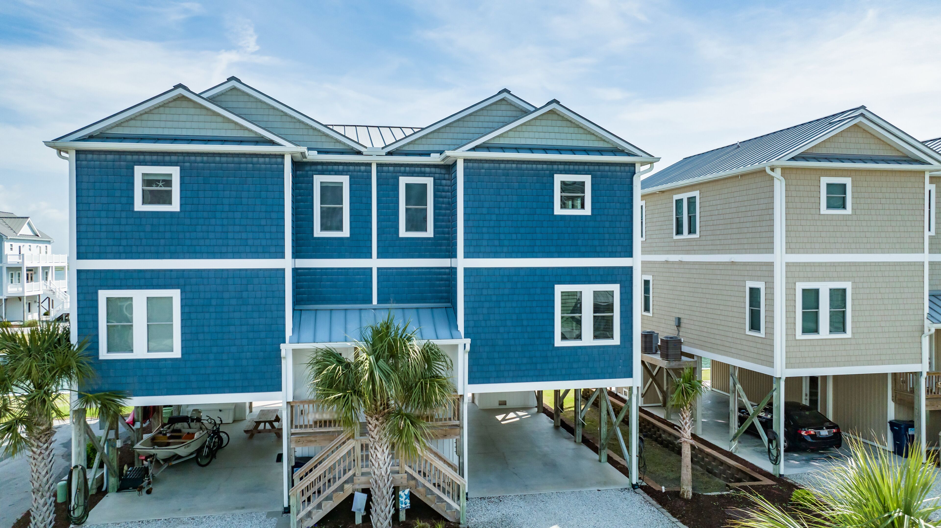 A two-story house with a blue exterior and a beige exterior. There is a covered patio area with a wooden deck and a small boat.