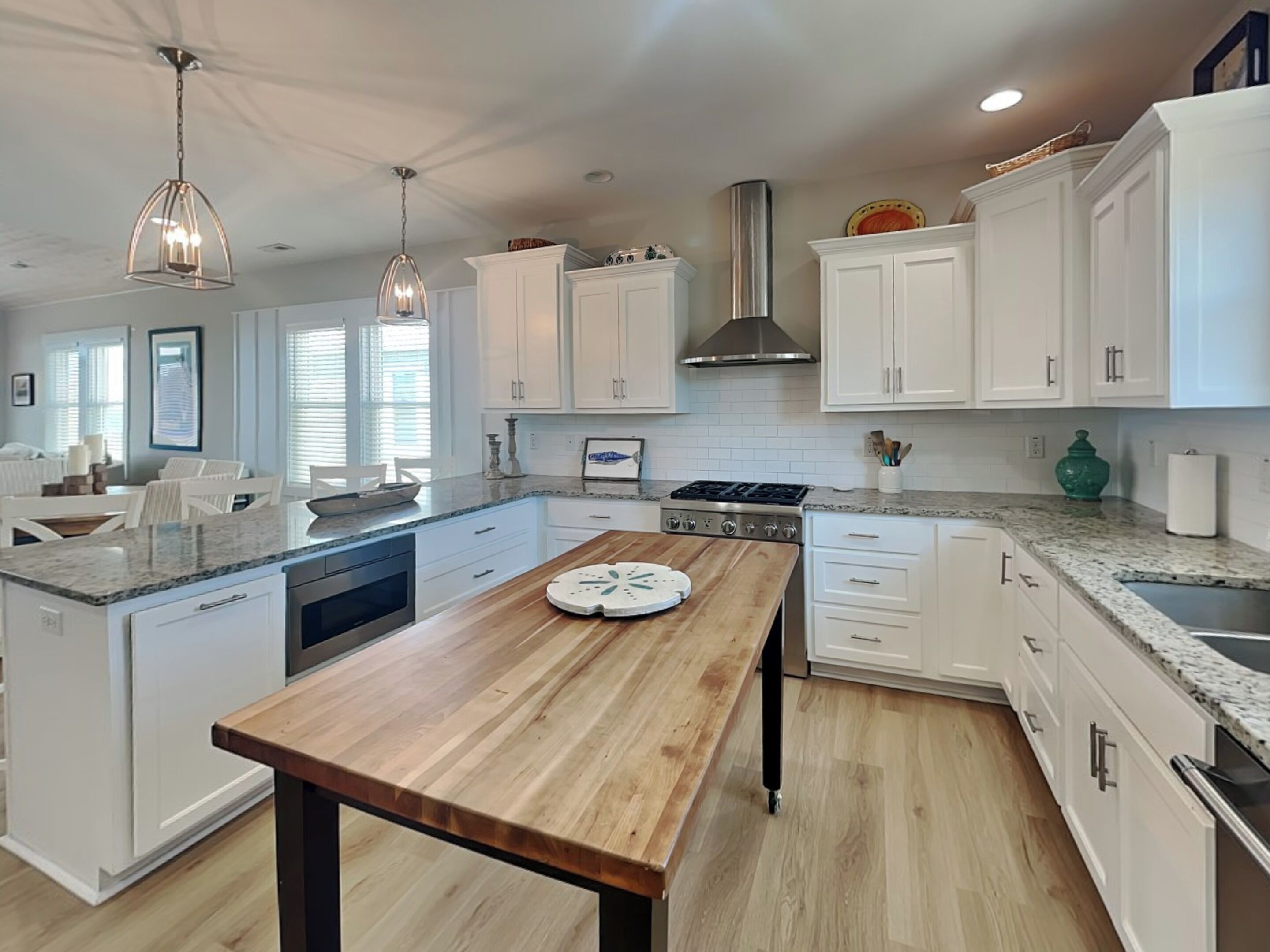 A modern kitchen with white cabinetry, a wooden island, stainless steel appliances, and pendant lighting.