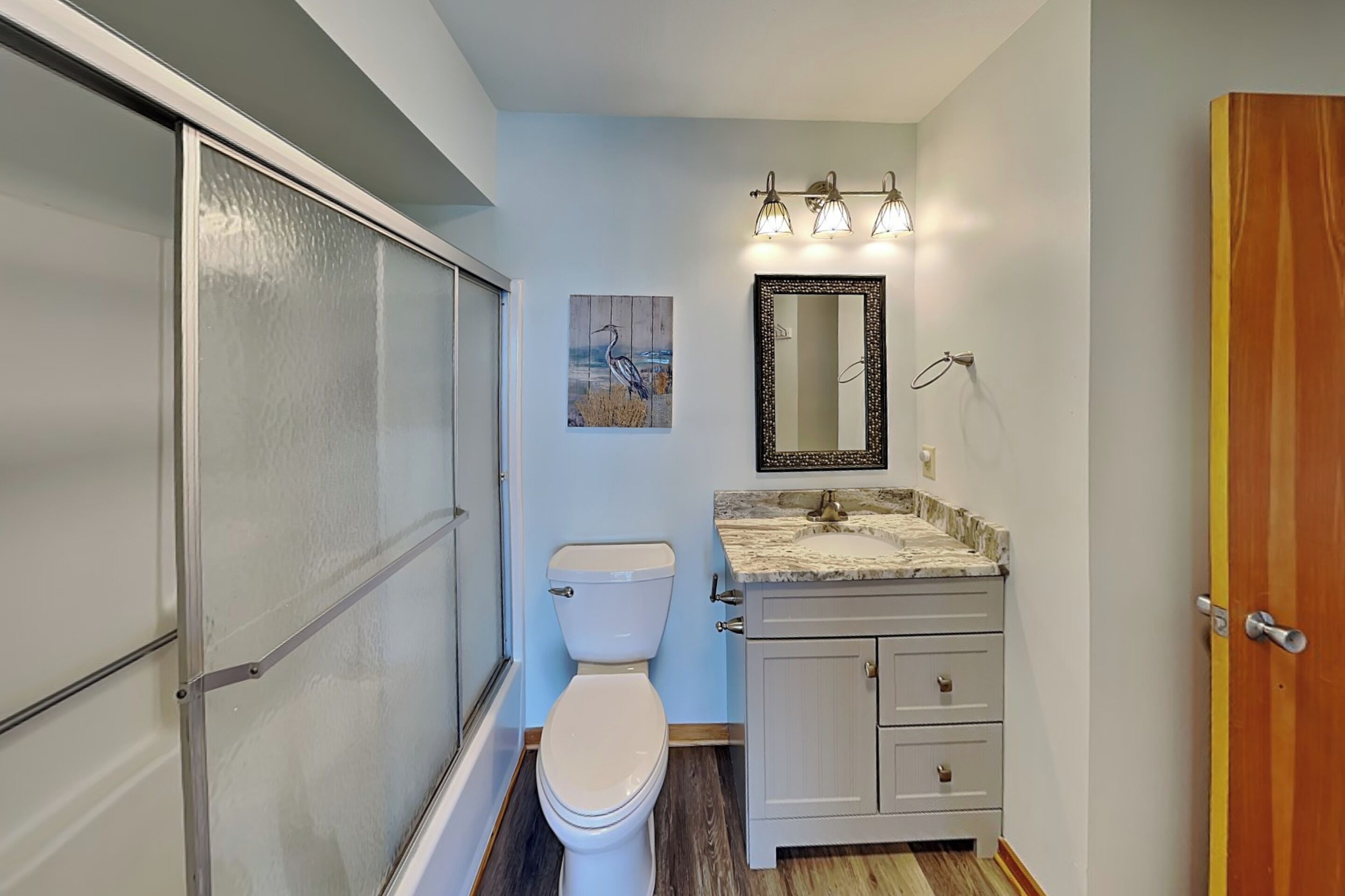 A bathroom with a toilet, vanity, mirror, and shower enclosure.