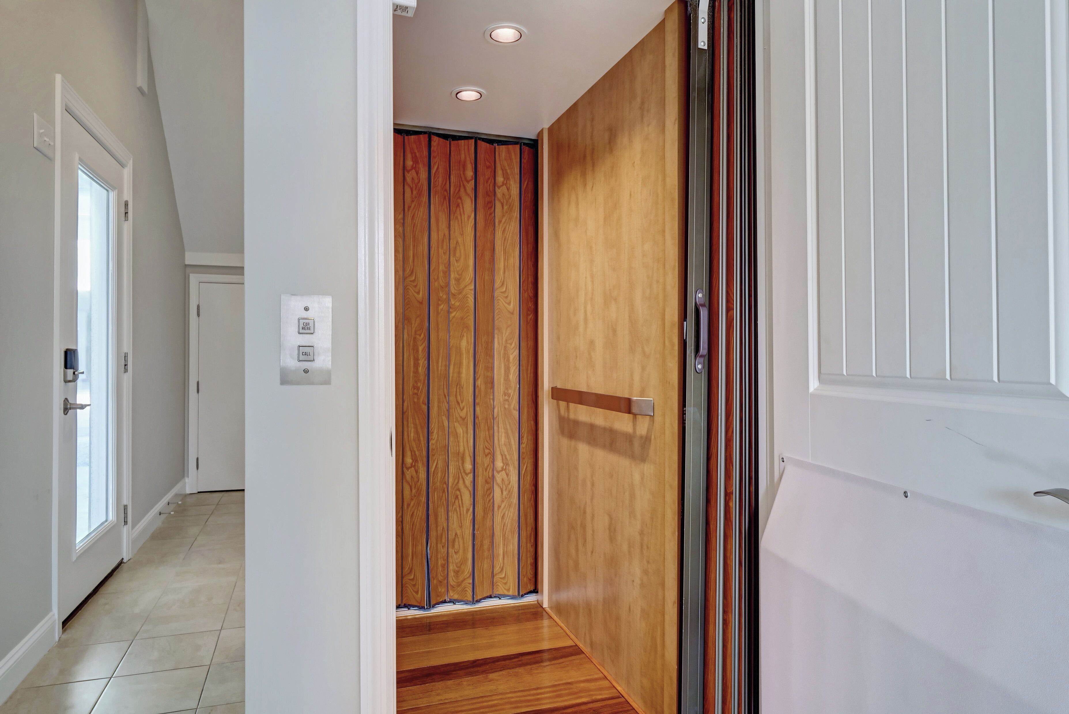 A hallway with a wooden door, a white door, and a light switch on the wall.