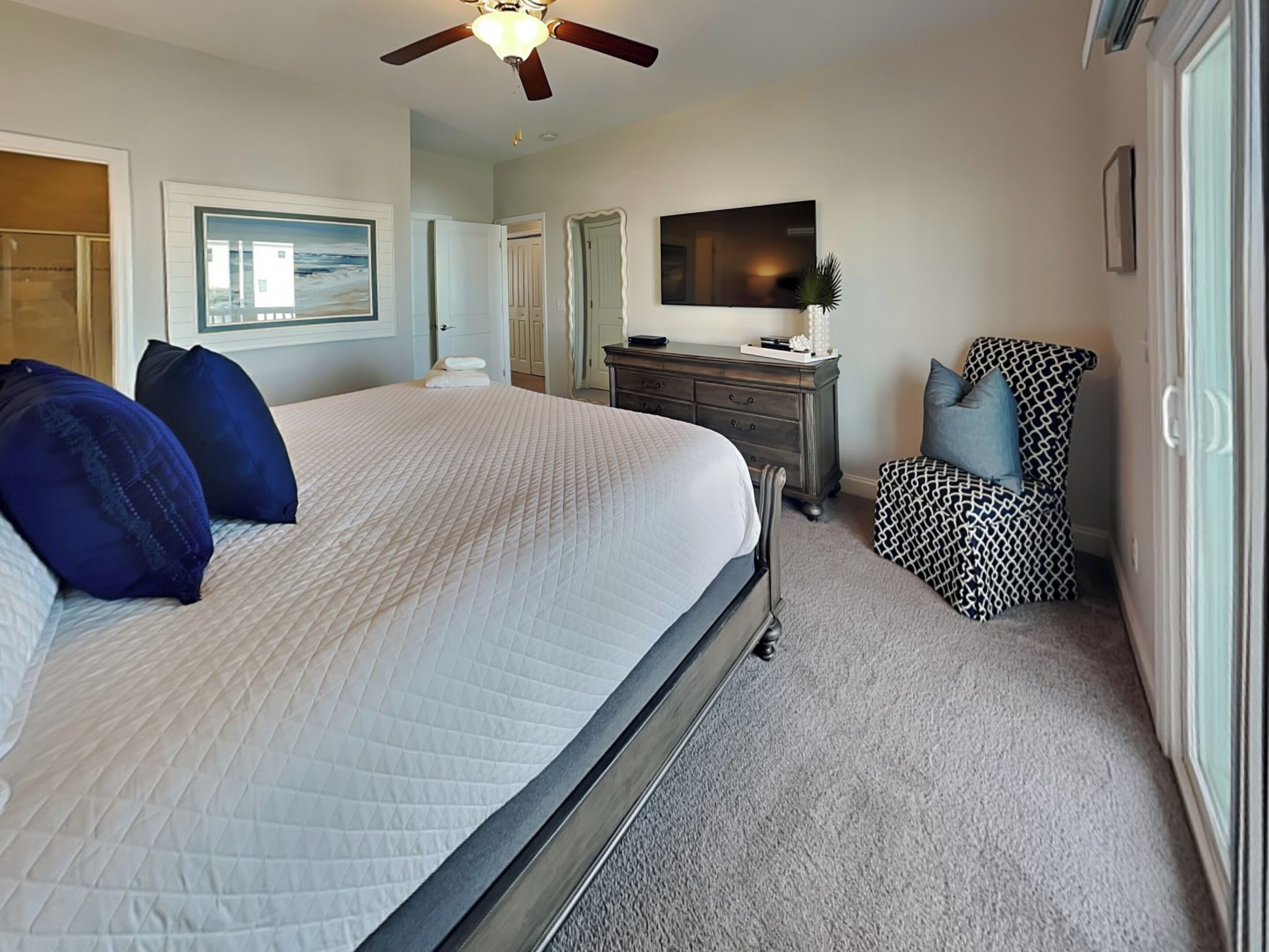 A bedroom with a large bed, a dresser, a chair, and a ceiling fan.
