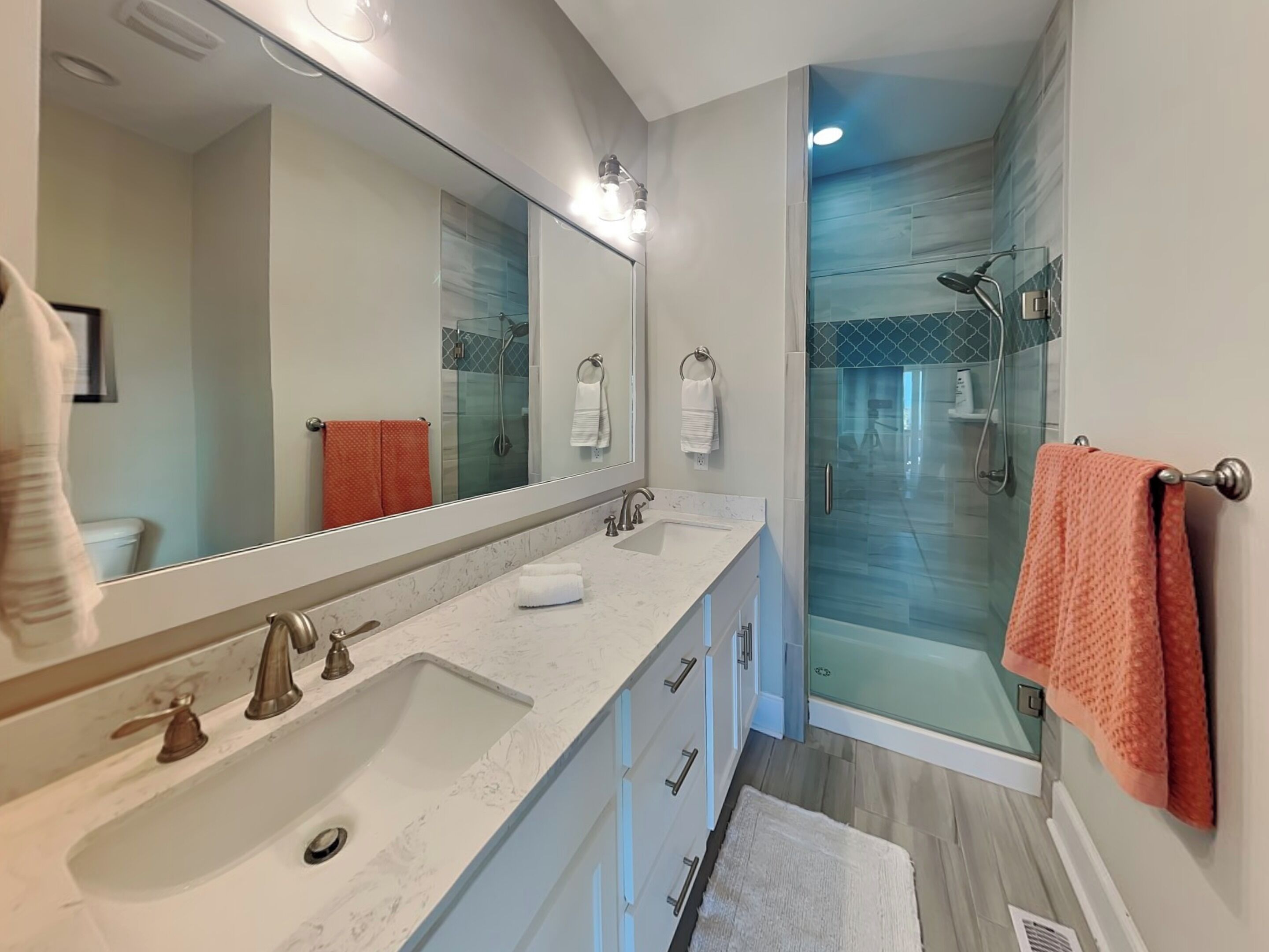 A modern bathroom with a large mirror, a double sink, and a glass-enclosed shower area.