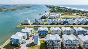 A coastal residential area with multiple two-story houses, a marina, and a beach in the background. - Queens Grant by Topsail Realty (Holly Ridge)