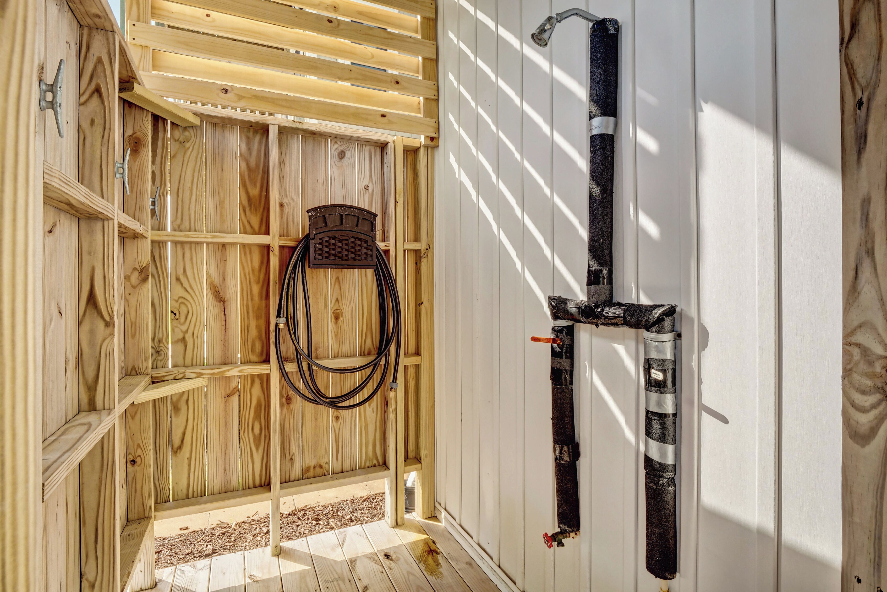 A wooden room with a slatted ceiling, a metal rack, and a hose.
