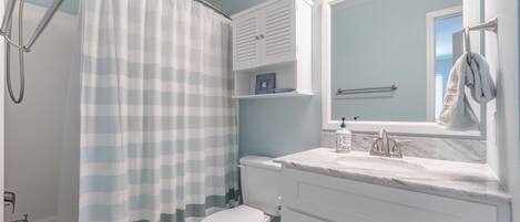 A bathroom with a shower curtain, toilet, sink, and vanity.