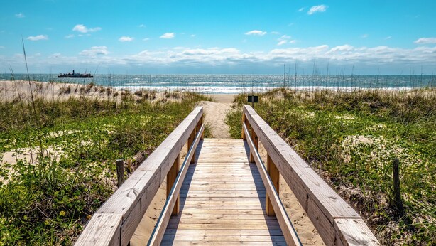 A wooden boardwalk leading to a beach with a ship in the distance. - Coral Surf #A1 - Beachy Keen by Carolina Retreats (Carolina Beach)