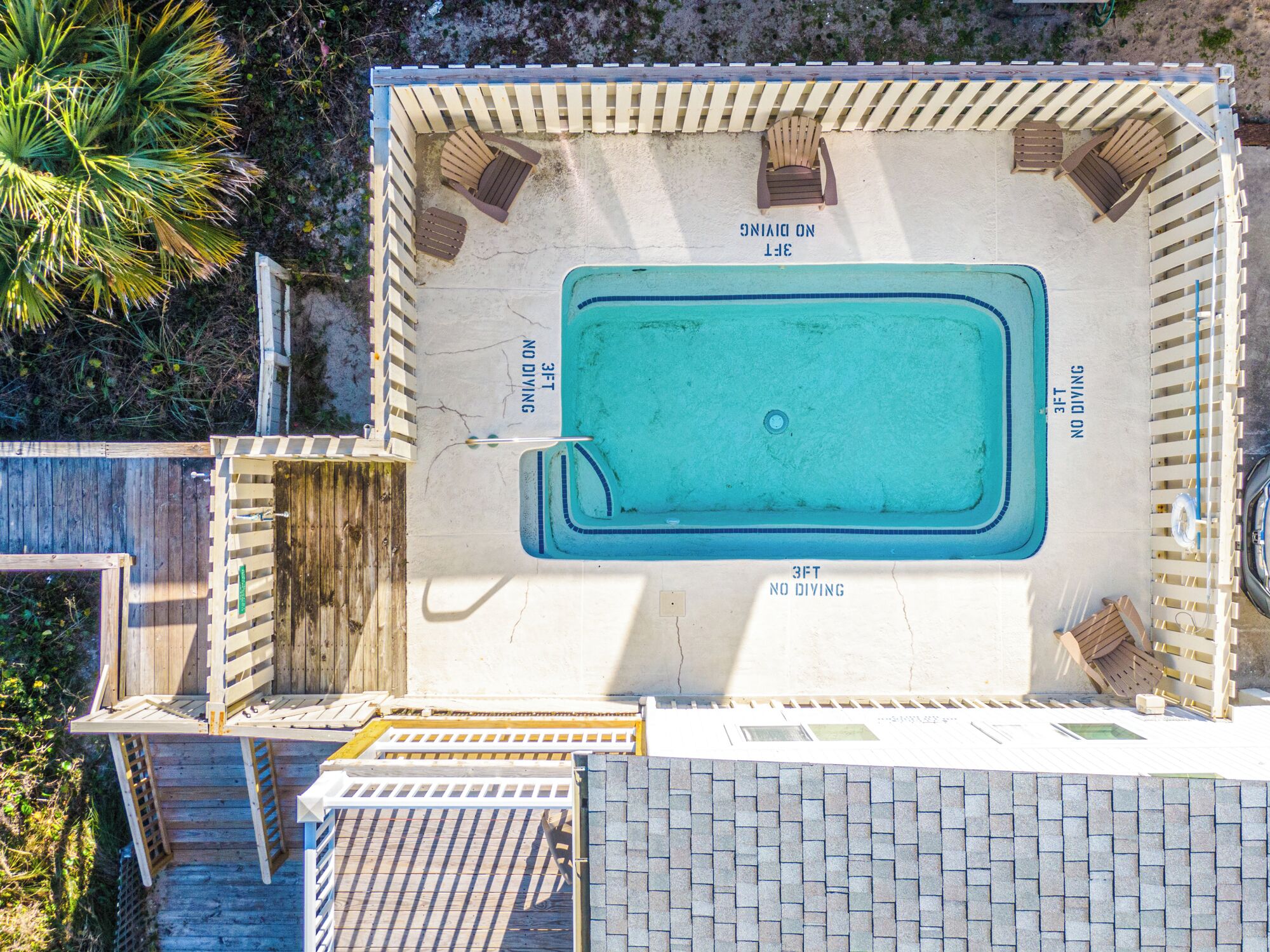 An aerial view of a rectangular pool with a 3ft no diving zone, surrounded by wooden deck chairs and a wooden fence.