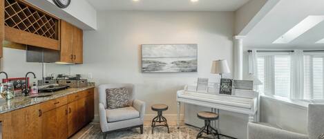 A modern kitchen with wooden cabinets, a built-in wine rack, a dining area with a piano, and a cozy seating arrangement.