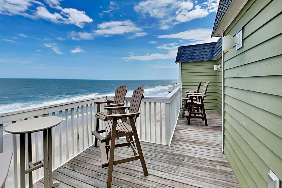 A wooden deck with chairs and a table overlooking the ocean.