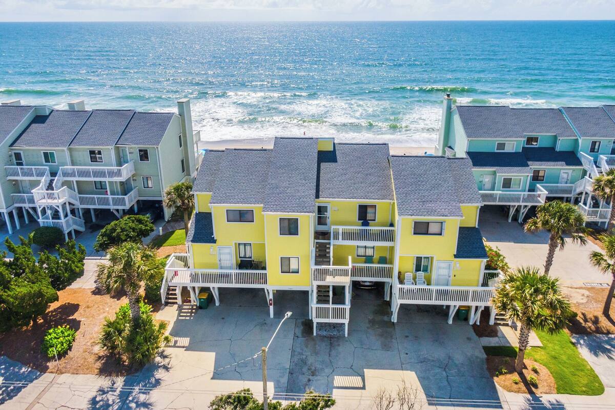 A beachfront hotel with multiple-story buildings, balconies, and a view of the ocean.