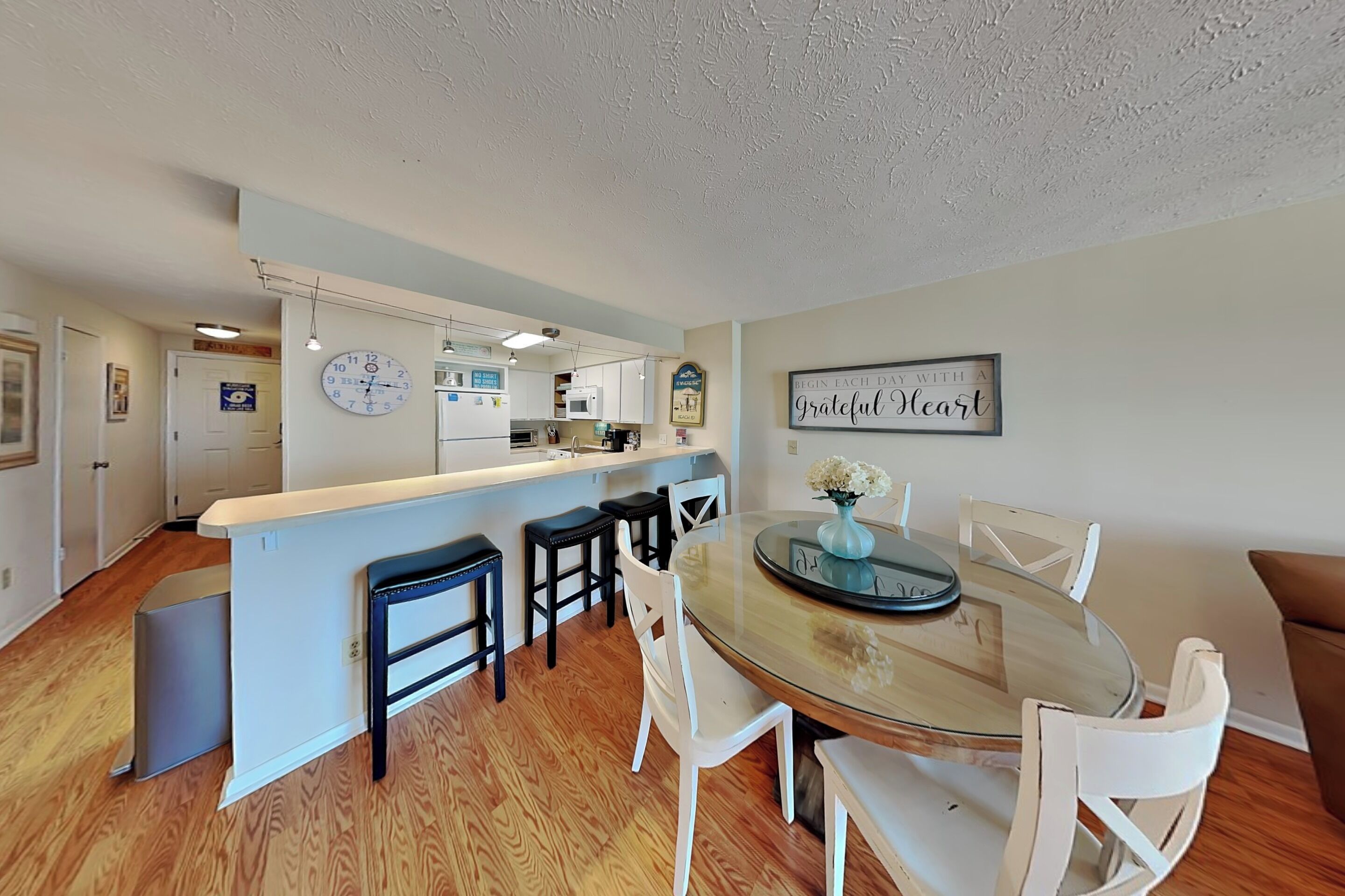 A modern kitchen with white cabinets, a central island, and a dining area with a glass table and white chairs.