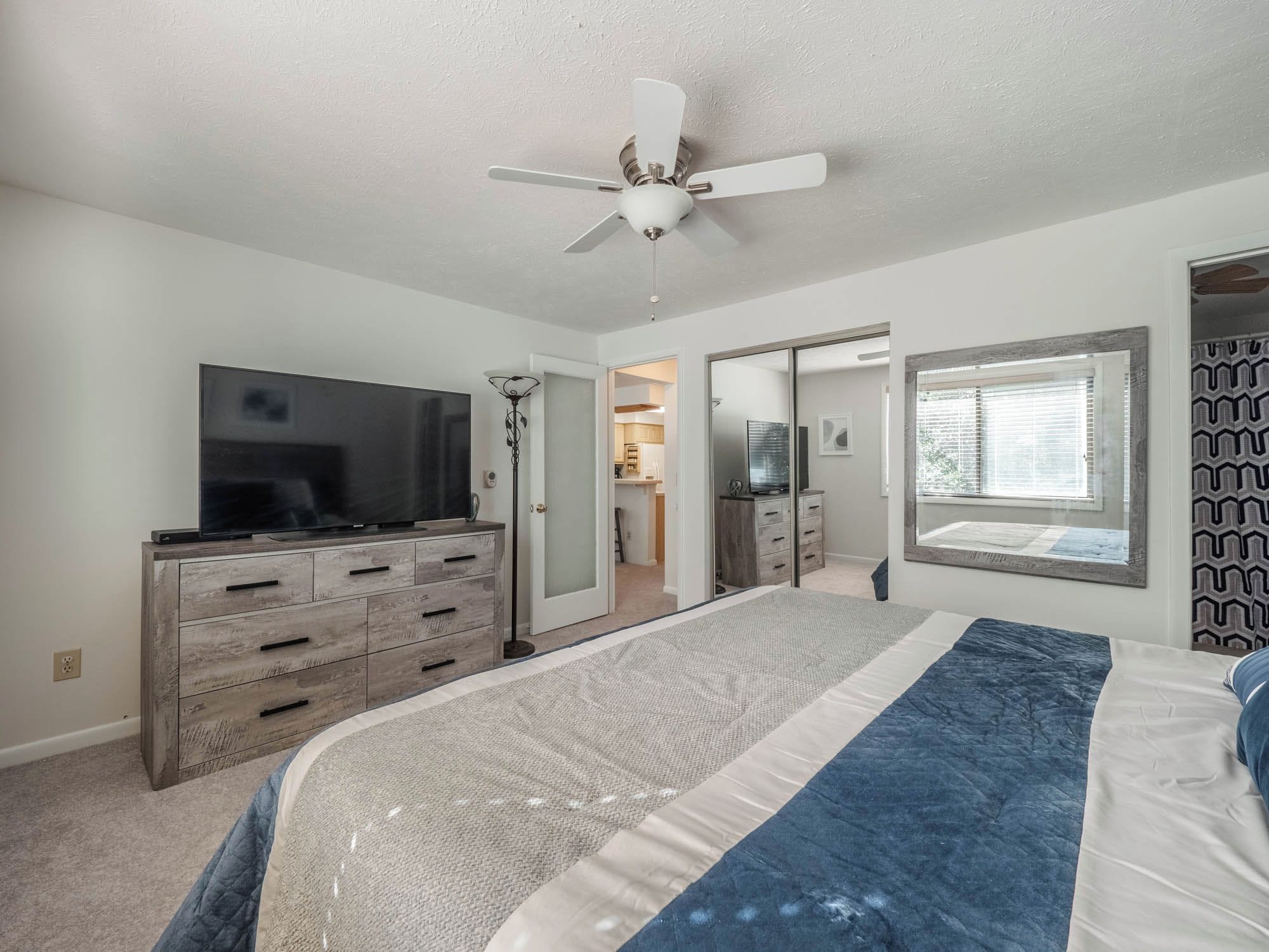 Ein Schlafzimmer mit Bett, Fernseher, Kleiderschrank, Deckenventilator und Fenster.