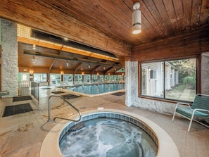 A spa area with a hot tub, wooden ceiling, stone walls, and a view of a house. - Ocean Dunes by Carolina Retreats (Kure Beach)