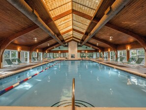 An indoor swimming pool with a wooden ceiling and stone walls, surrounded by lounge chairs. - Ocean Dunes by Carolina Retreats (Kure Beach)