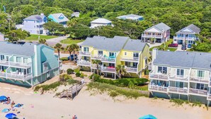 A coastal residential area with beachfront properties, including houses with balconies and a beach with umbrellas and people. - Ocean Dunes by Carolina Retreats (Kure Beach)