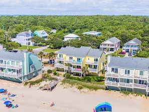 A coastal residential area with beachfront properties, including houses with balconies and a beach with umbrellas and people. - Ocean Dunes by Carolina Retreats (Kure Beach)