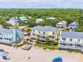 Zona residencial costera con propiedades frente al mar, incluyendo casas con balcones y una playa con sombrillas y gente.