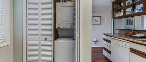 A laundry room with a washer and dryer, a wooden cabinet with dishes, and a white door.