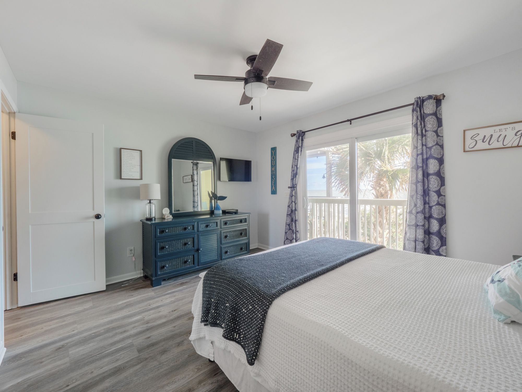 A bedroom with a bed, a dresser, a ceiling fan, and a window with curtains.