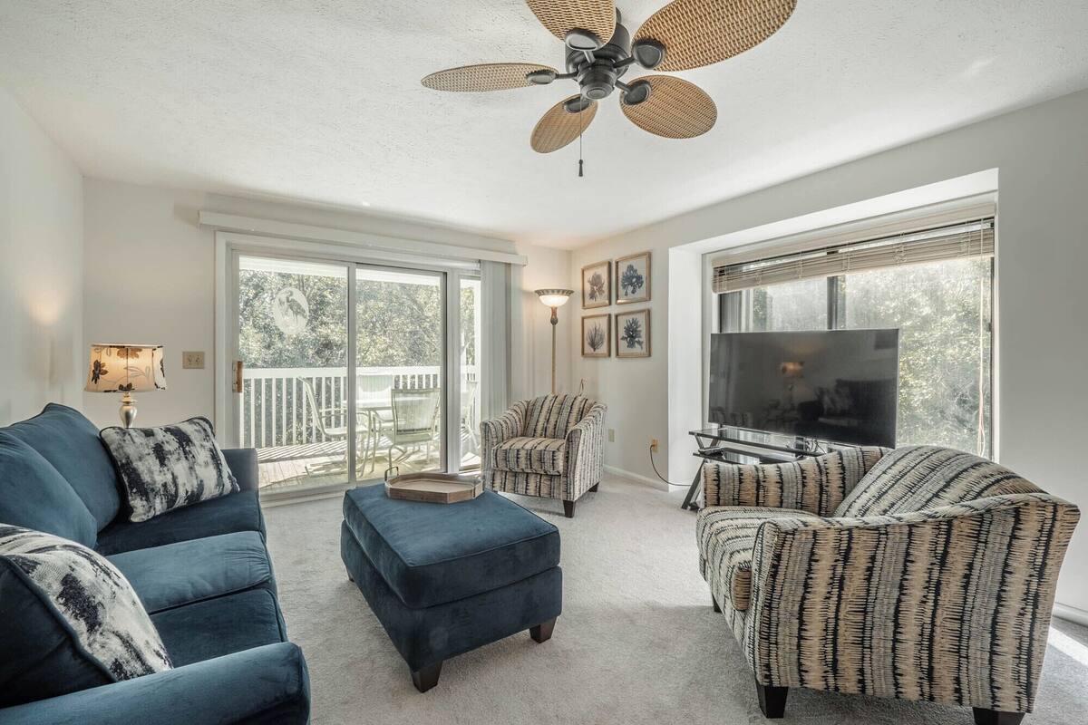 A living room with a ceiling fan, a TV, and a large window.