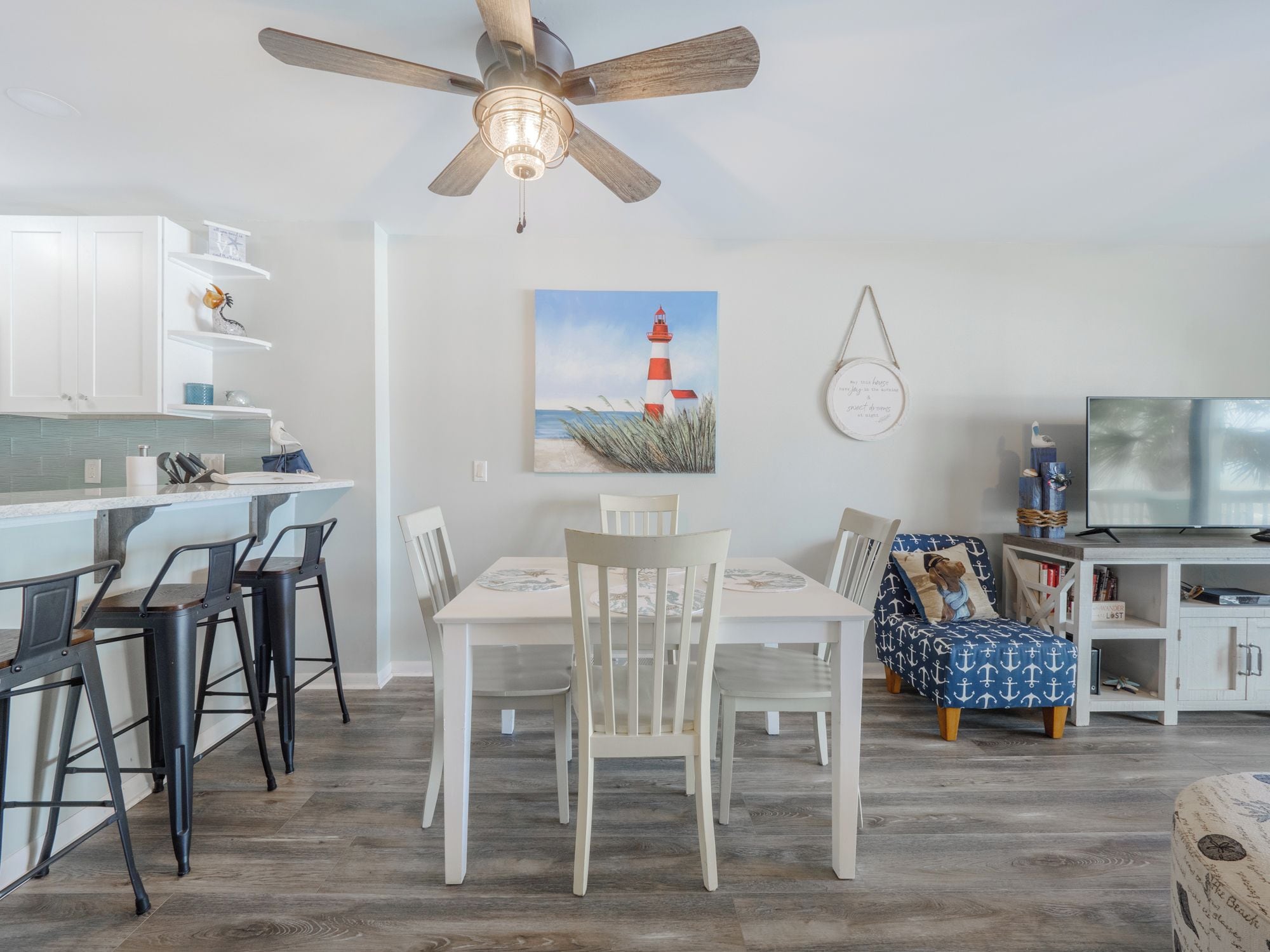 Une cuisine moderne avec des armoires blanches, un ventilateur de plafond en bois et un coin repas comprenant une table et des chaises blanches.