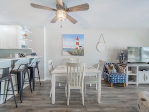 Une cuisine moderne avec des armoires blanches, un ventilateur de plafond en bois et un coin repas comprenant une table et des chaises blanches.