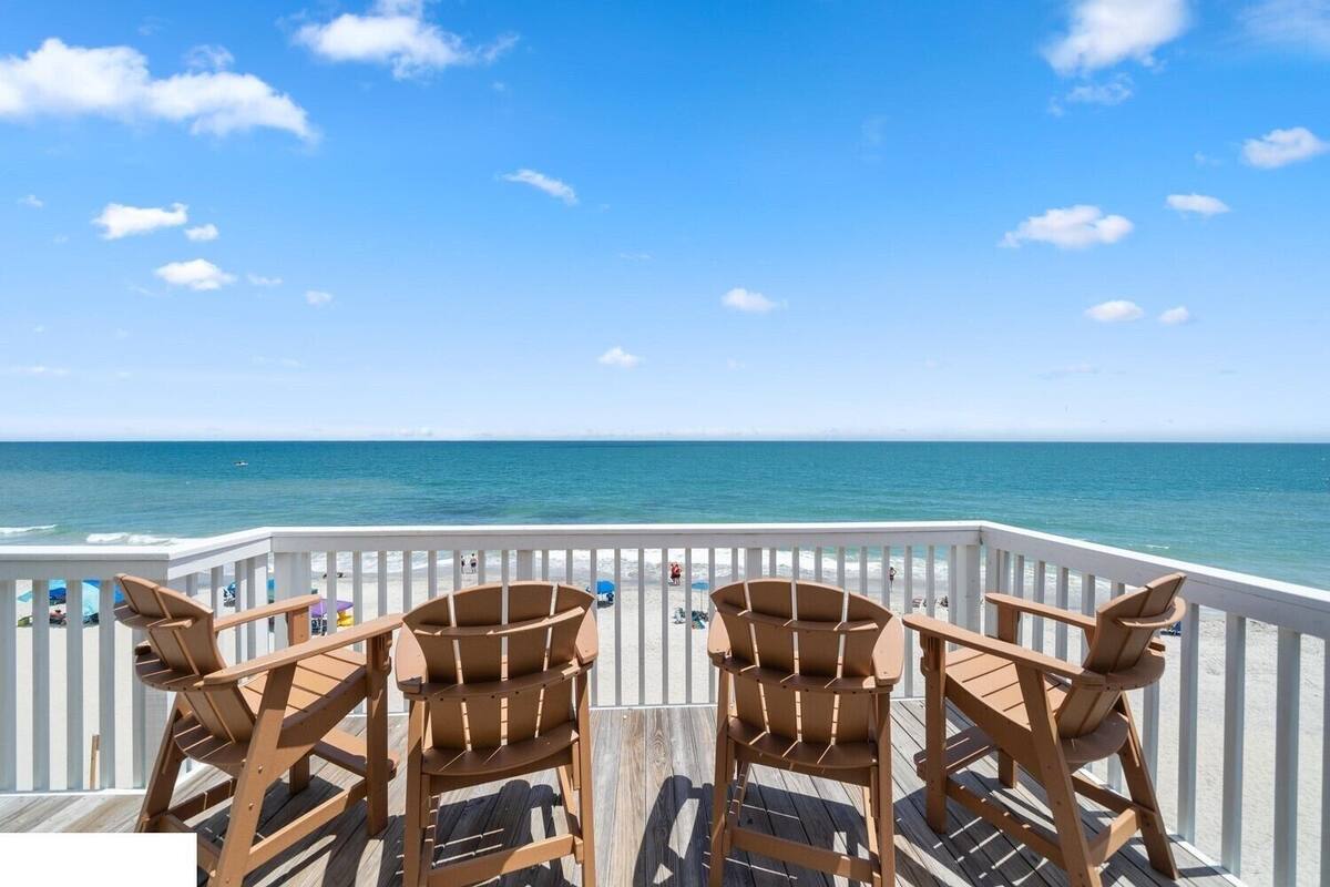 A wooden deck with two chairs facing a beach.