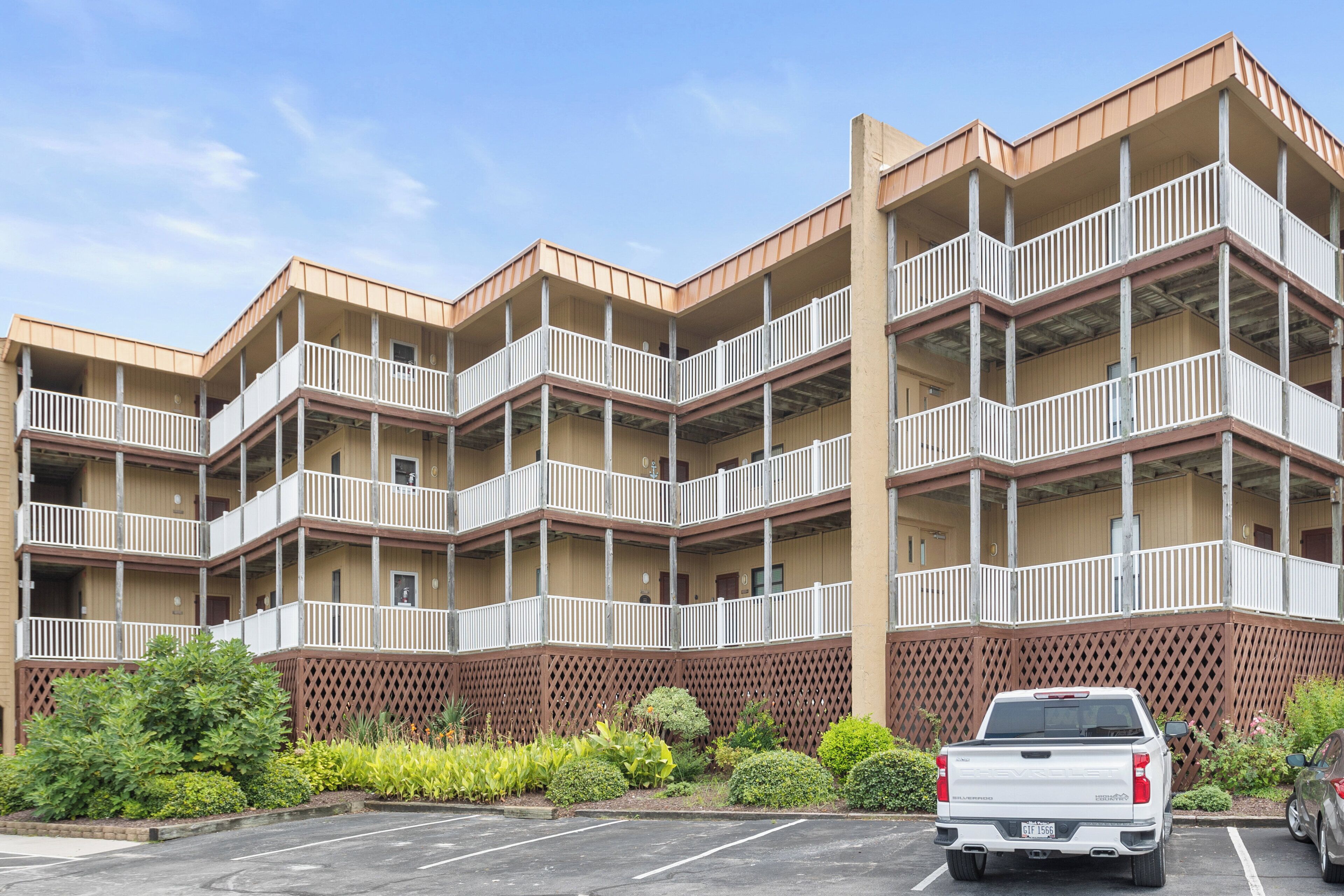 A multi-story hotel with balconies, a parking lot, and a white pickup truck parked in front.