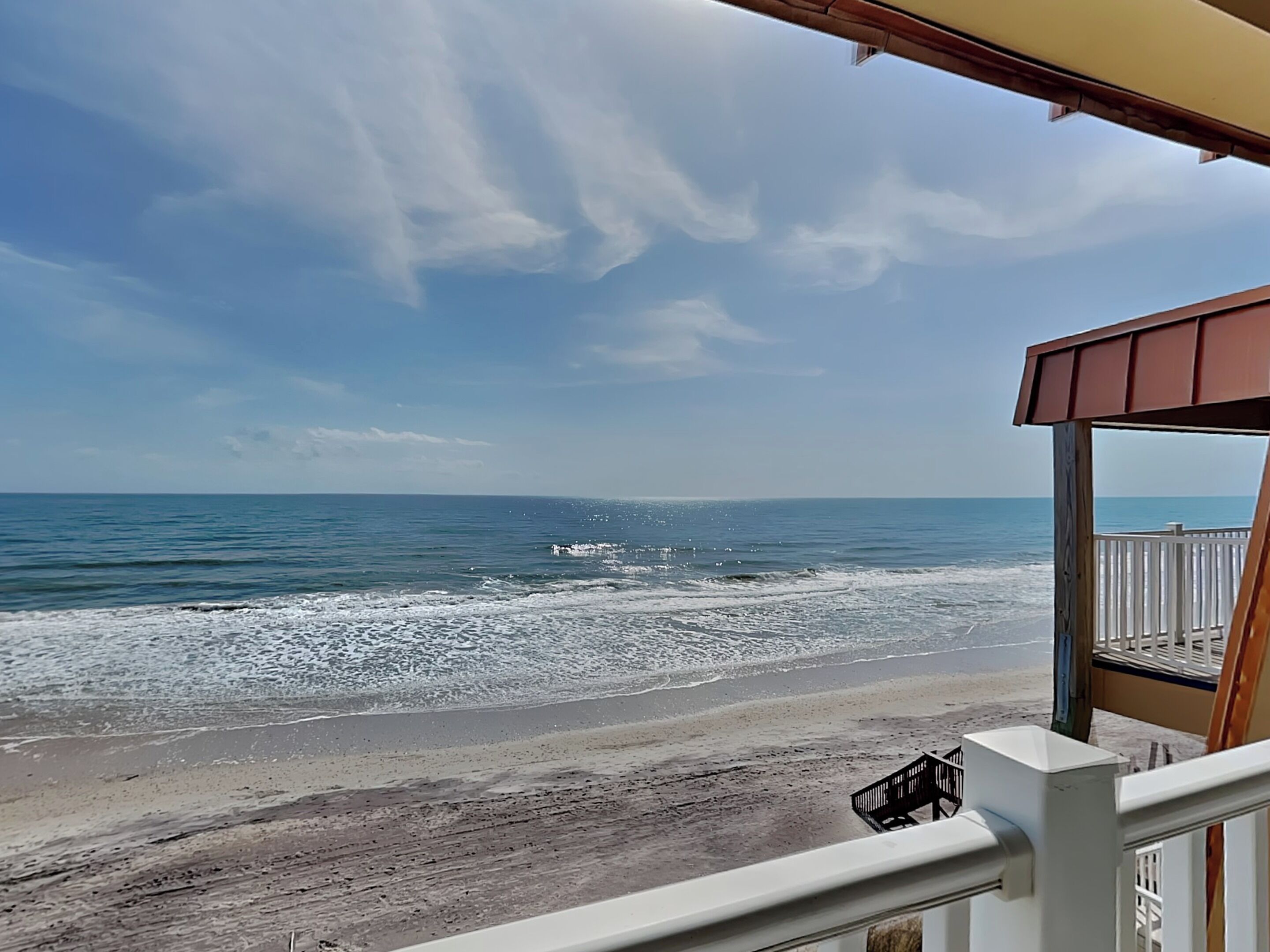 Vista al mar desde un balcón con barandilla de madera y un pequeño banco.