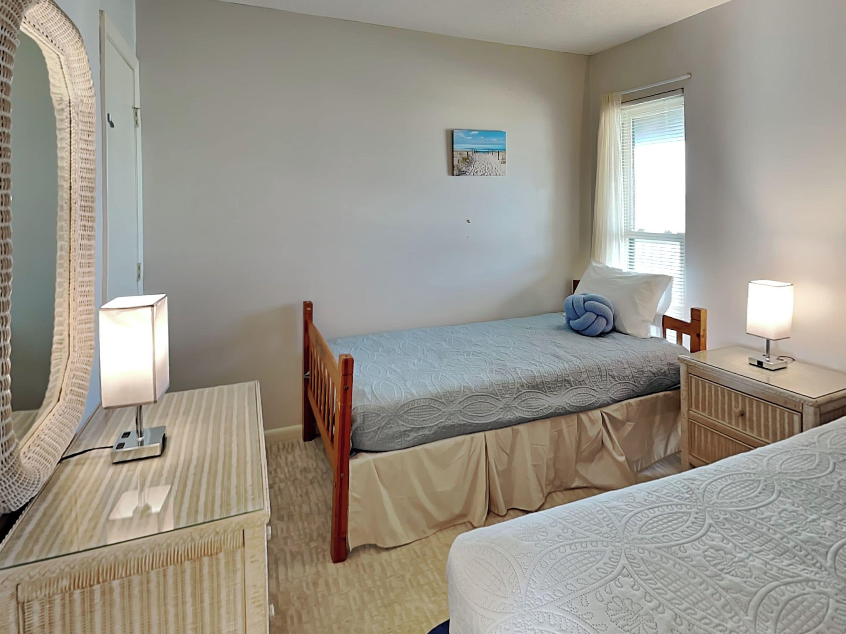Quarto com uma cama de solteiro, mesa de cabeceira com abajur, espelho e janela com persianas.