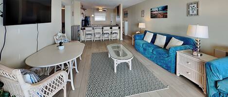 A living room with a blue sofa, a coffee table, and a dining area with chairs and a table.