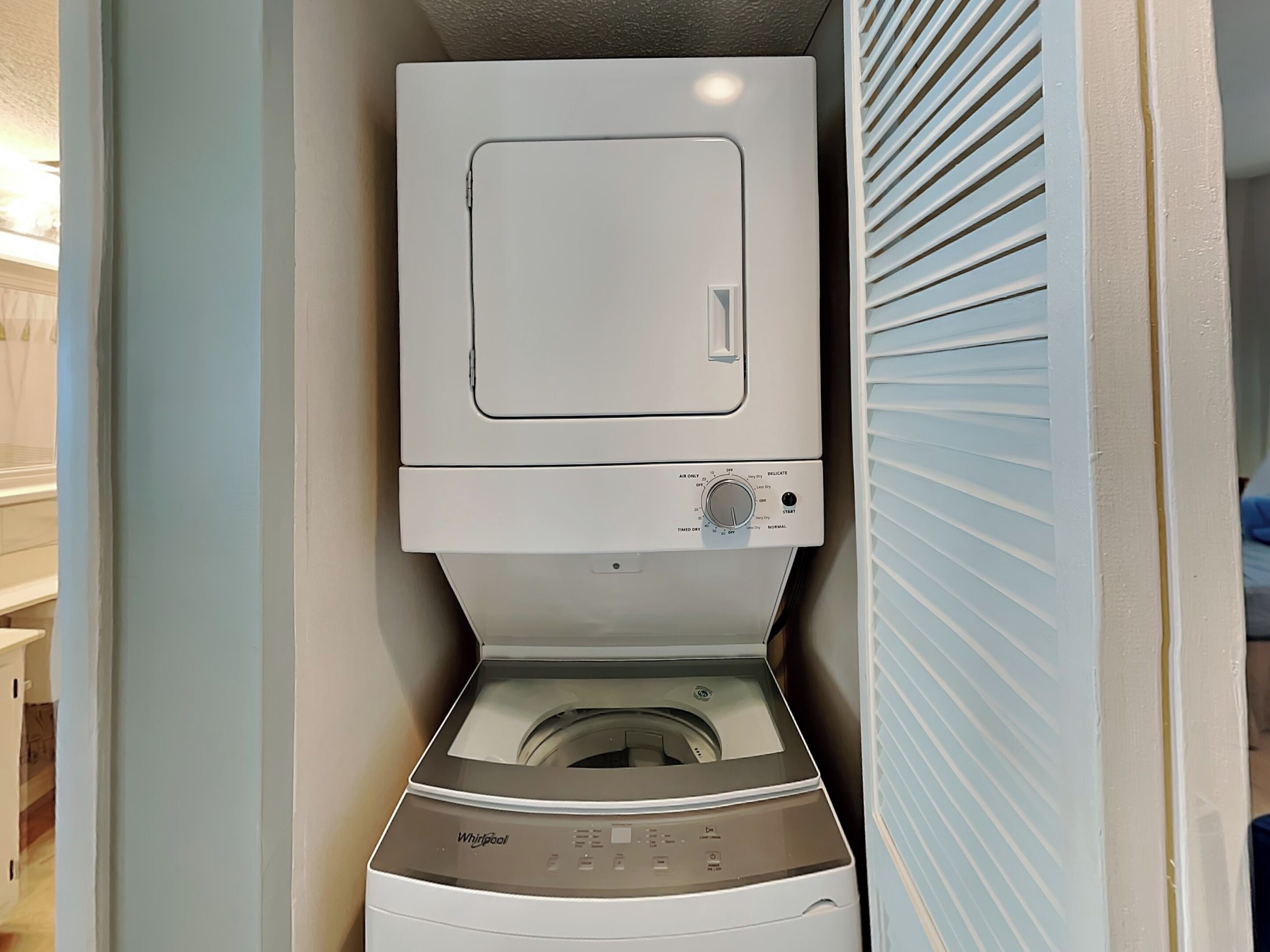 Una lavadora y secadora compactas, de montaje en pared, en un cuarto de lavado con puerta y ventana.