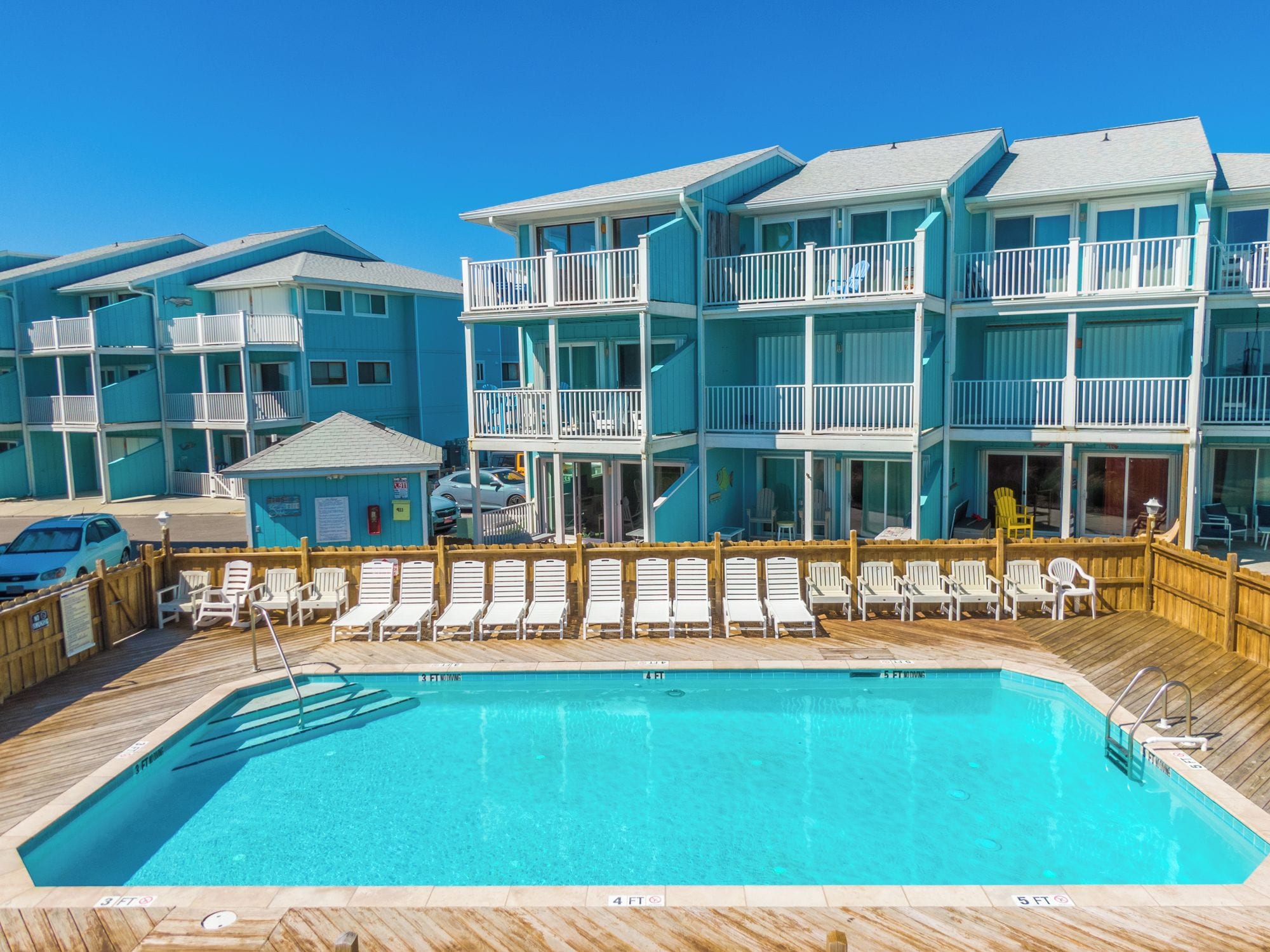 A hotel with a pool area, multiple balconies, and a wooden deck with lounge chairs.