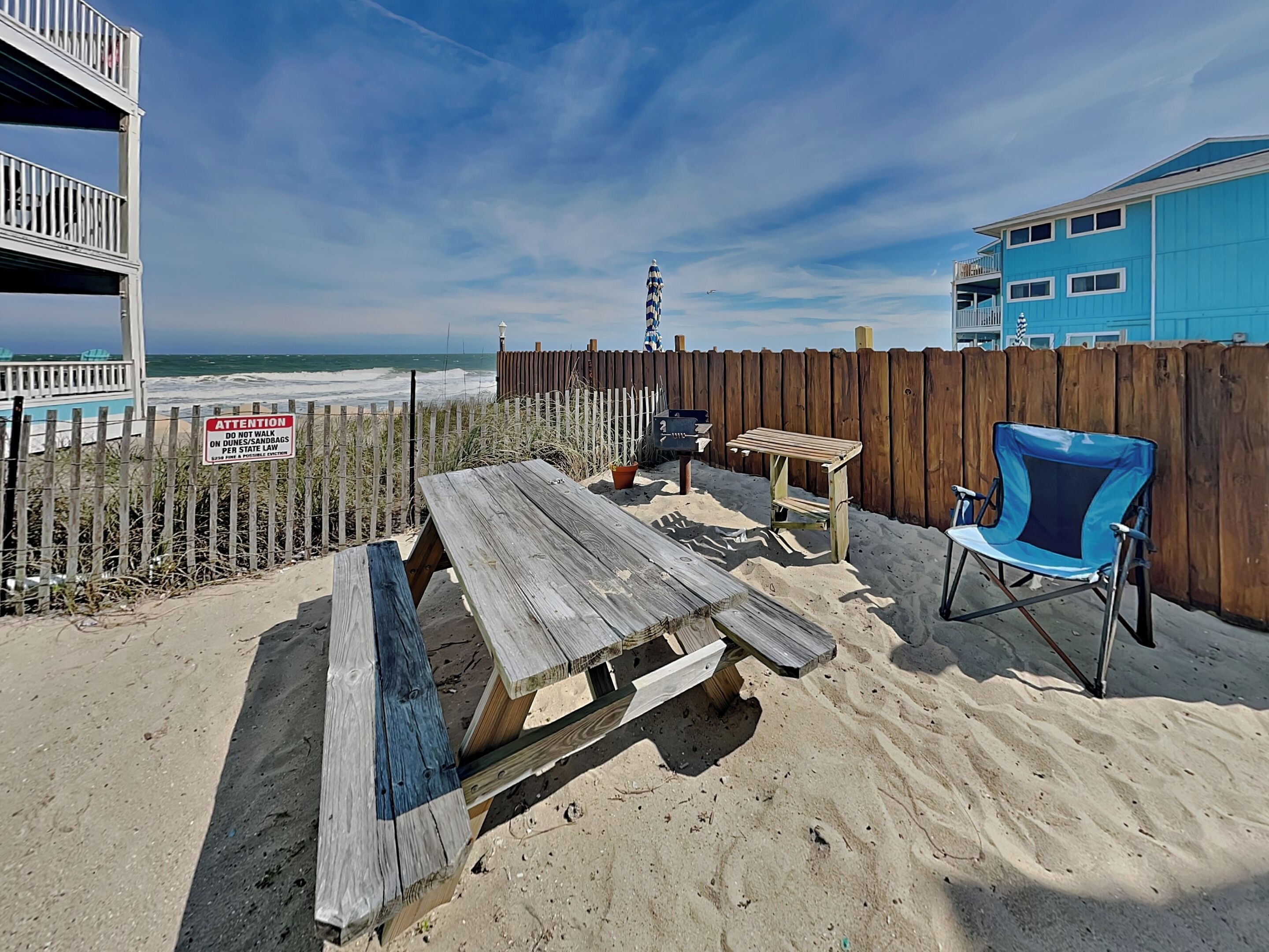 A beachside patio with a wooden table, a folding chair, and a wooden fence.