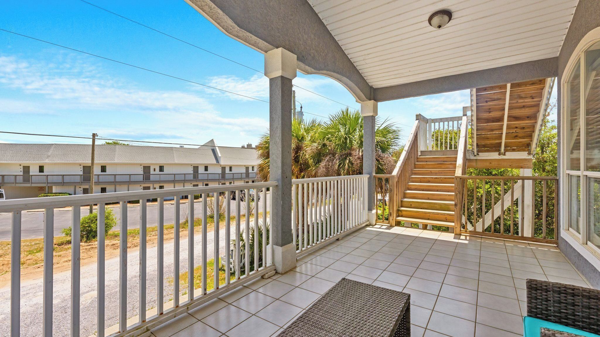 A covered balcony with a wooden staircase, tiled flooring, and a view of neighboring buildings.