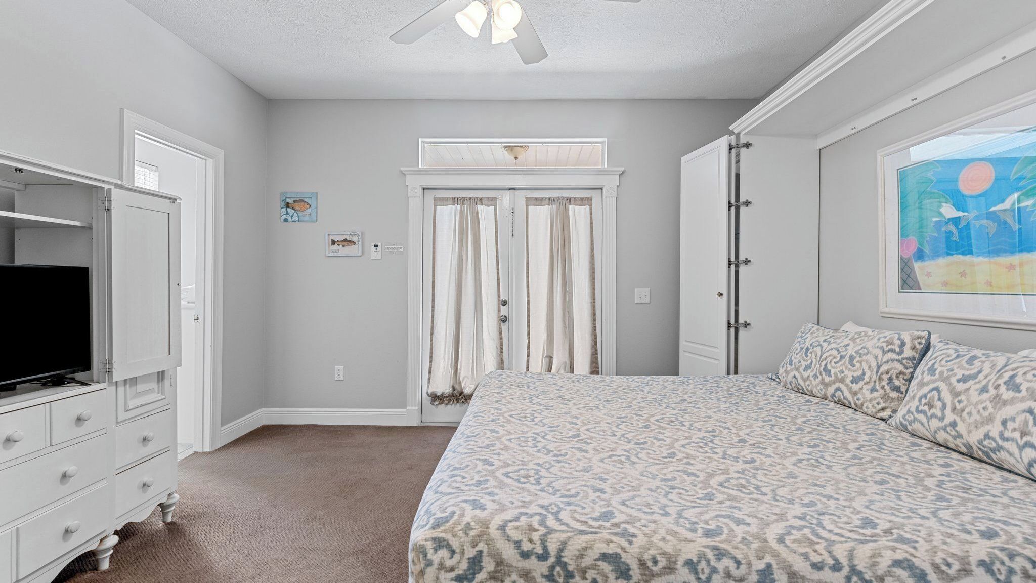 A bedroom with a bed, a television, a dresser, a closet, and a window with a painting.