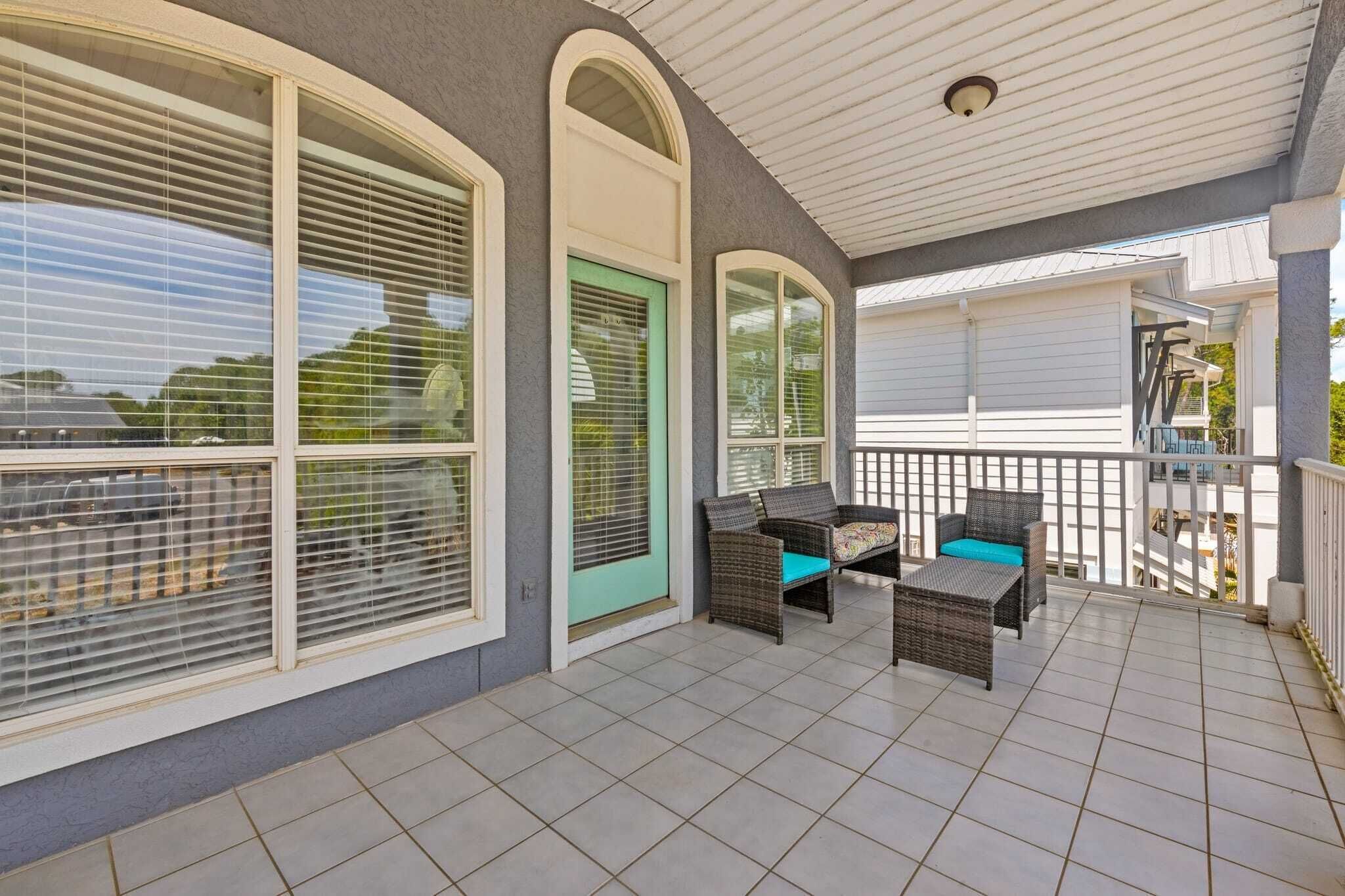 A covered patio with a tiled floor, a door with a green frame, and wicker furniture.