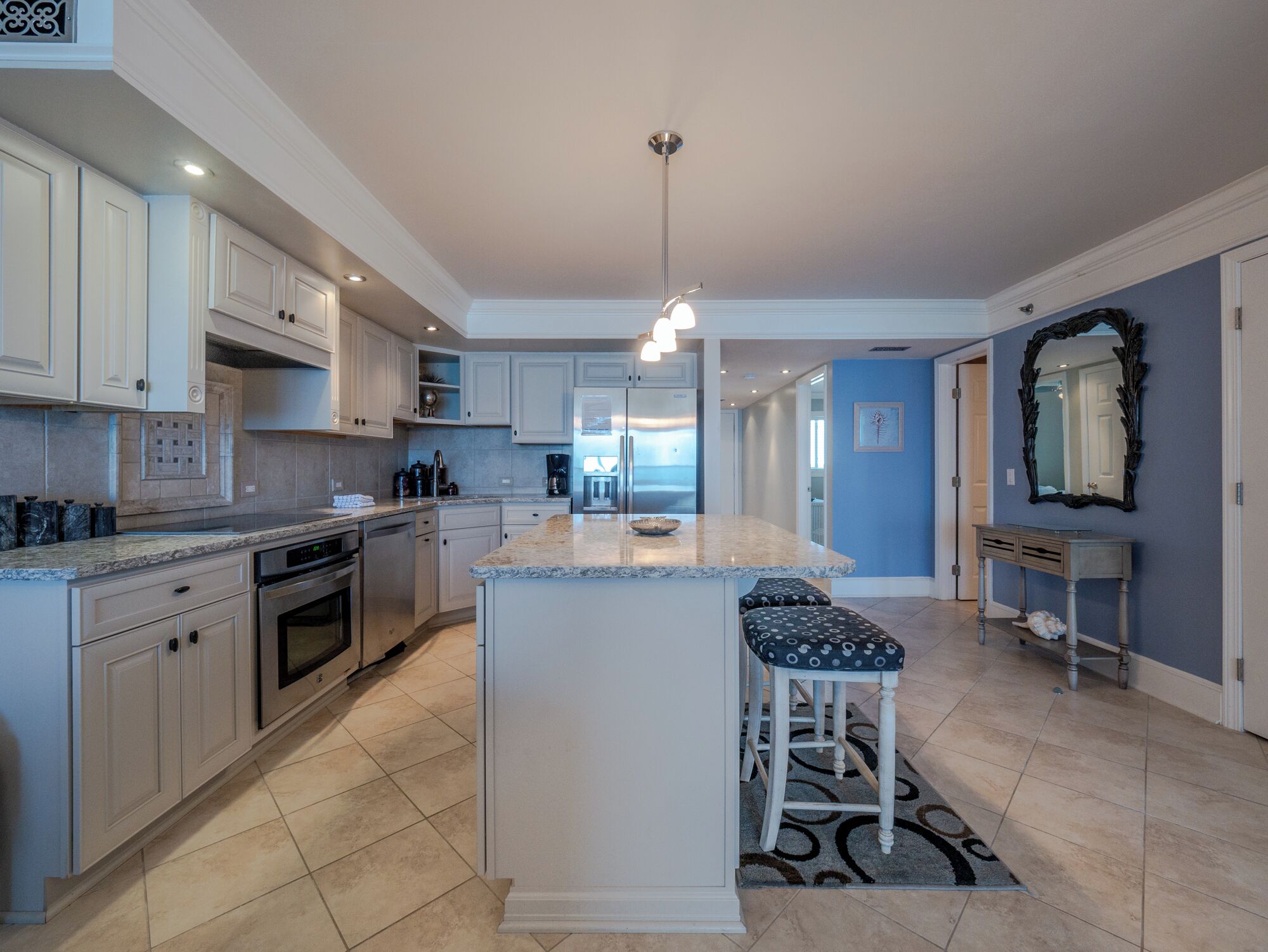A modern kitchen with white cabinetry, a granite countertop, and a central island with bar stools.