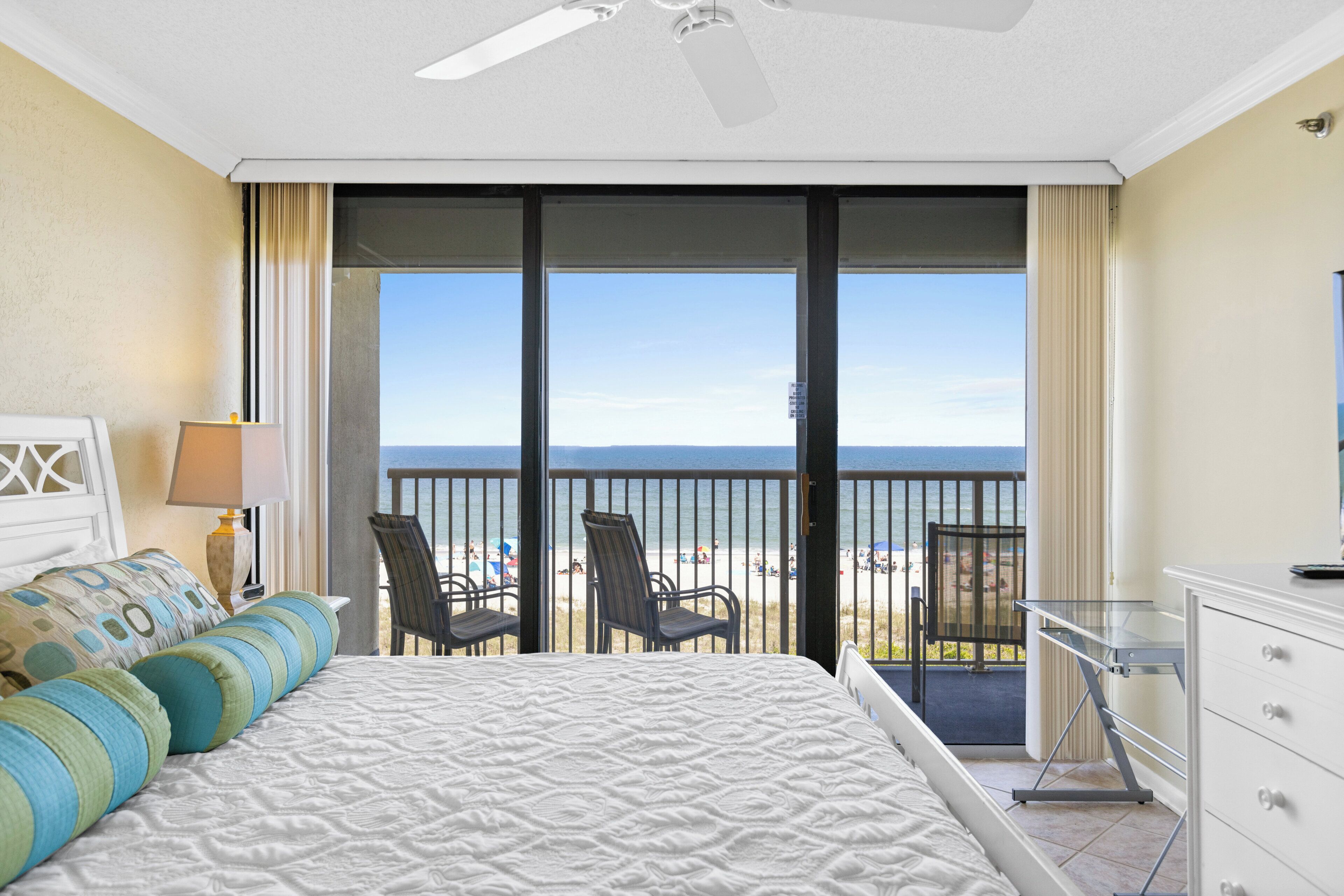 A hotel room with a large bed, a desk, and a view of the beach.