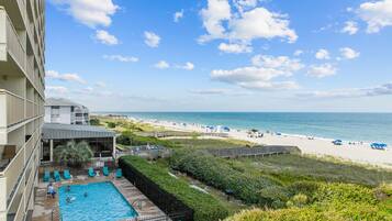 A hotel with a swimming pool, beach view, and a deck area.