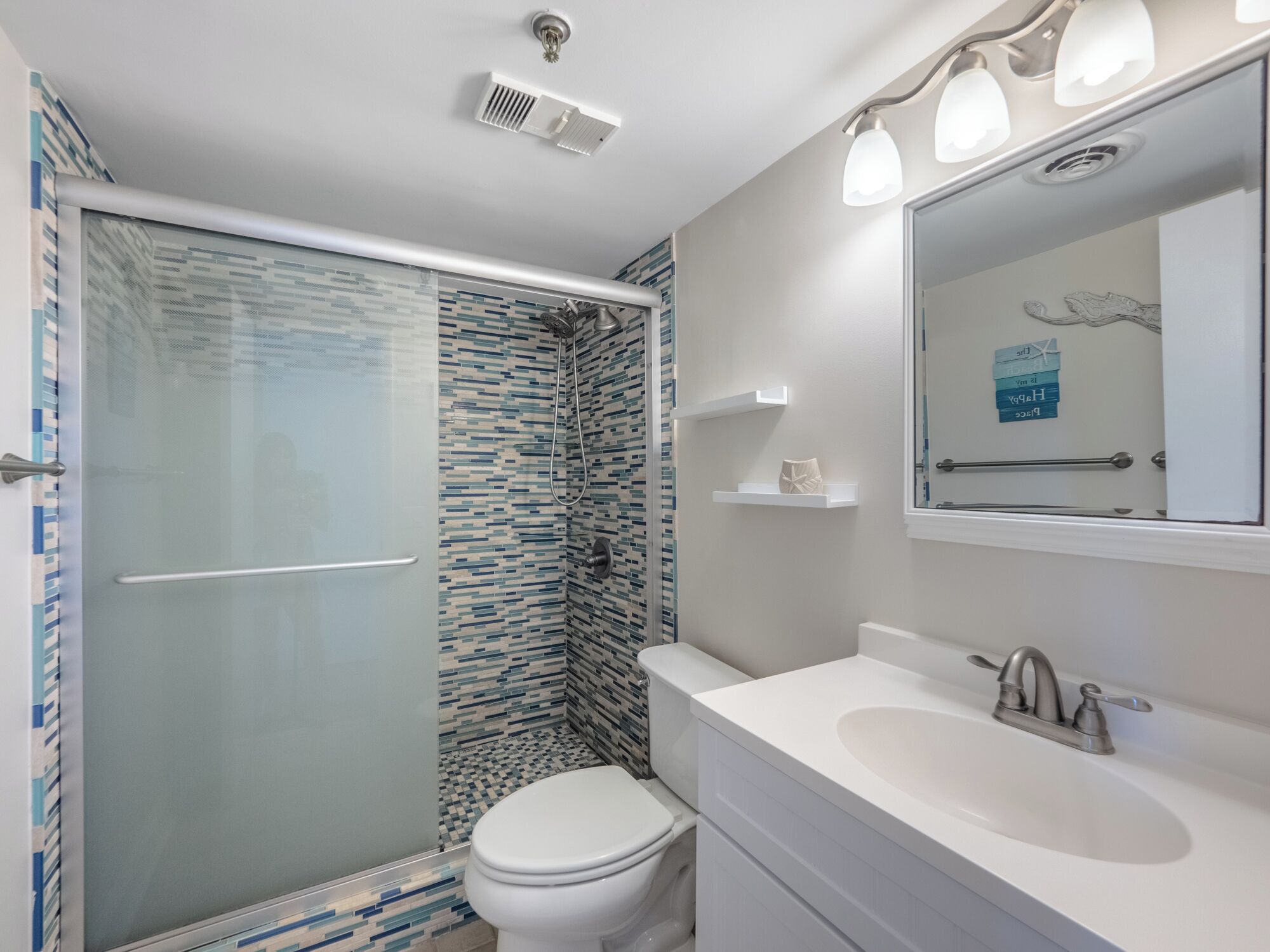 Ein Badezimmer mit Duschkabine aus Glas, einer weißen Toilette, einem Waschbecken mit Spiegel und einer gefliesten Rückwand.