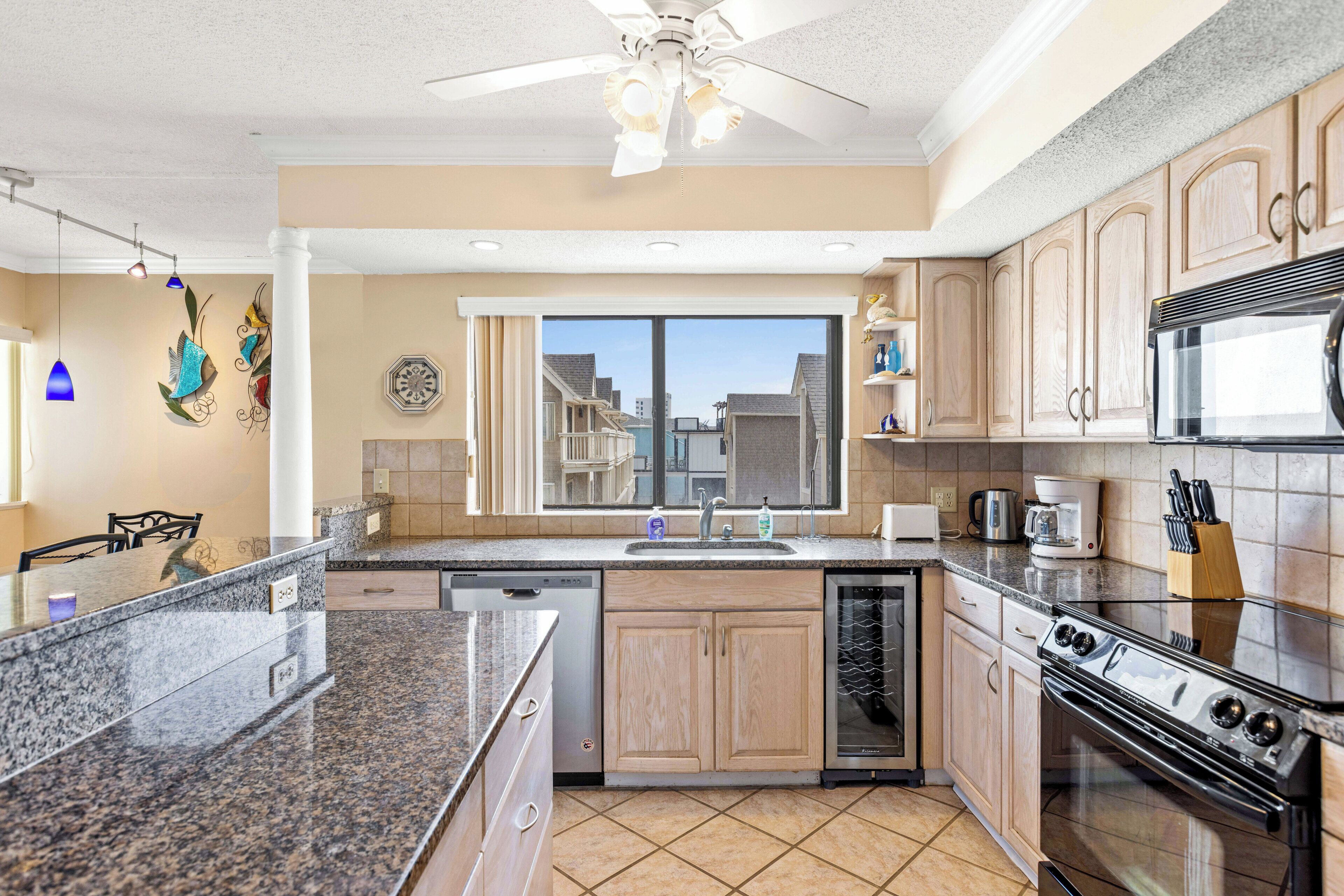 A modern kitchen with granite countertops, wooden cabinets, a dishwasher, a stove, and a large window offering a city view.