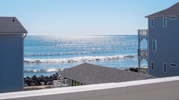 A beachfront property with a view of the ocean, a small dock, and a building with a balcony. - Sunskipper by Carolina Retreats (Carolina Beach)